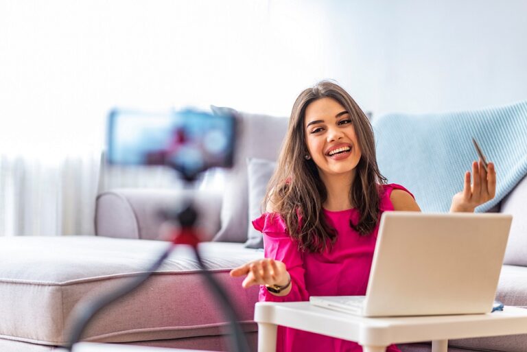 Woman sitting beside desk with laptop while filming her broadcast